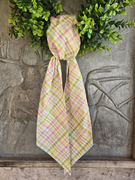 A plaid fabric sash tied in a bow, hanging on a door decorated with greenery.