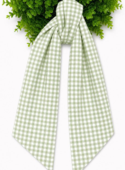 A light green and white gingham checkered sash, tied in a knot at the top and draped downward, set against a white background with green wreath at the top edge.
