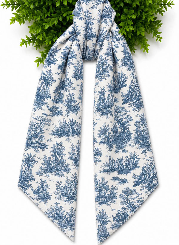 A white scarf with a blue toile de Jouy pattern, styled with green foliage at the top against a white background.